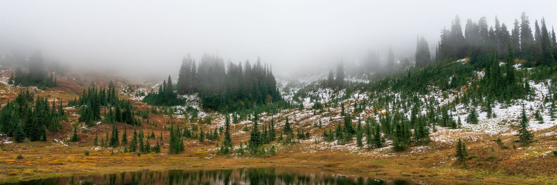 Fog over a small alpine lake below Mount Rainier, first snow on the meadow